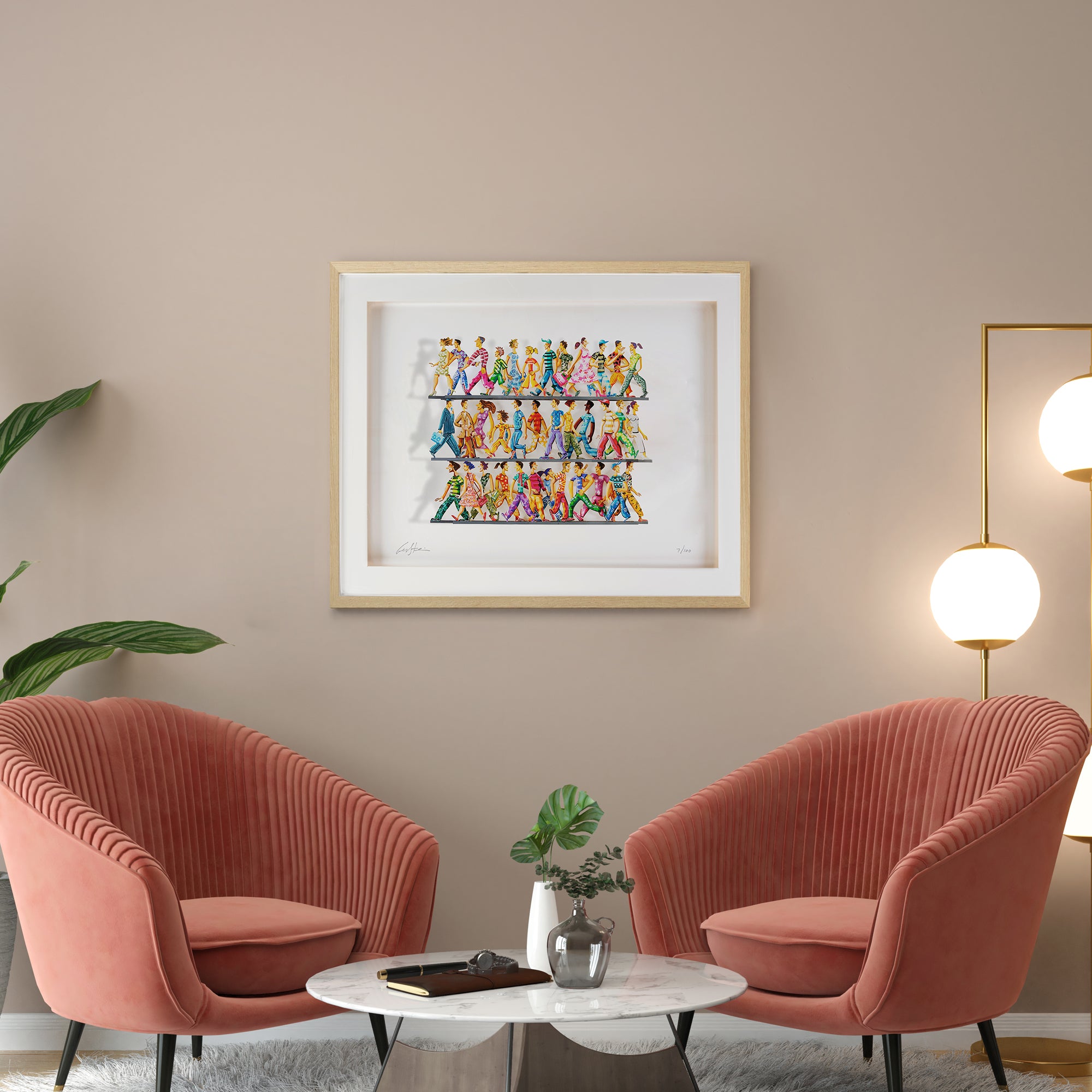 Framed hand-painted papercut artwork by David Gerstein, featuring colorful walking figures, mounted on a neutral wall above two pale pink chairs.