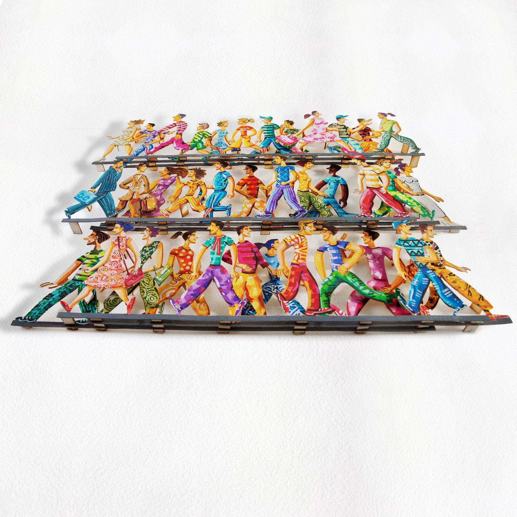 Angled full view of David Gerstein's hand-painted papercut artwork, showing colorful walking figures and revealing the depth of all three cut-out paper layers against a white backdrop.